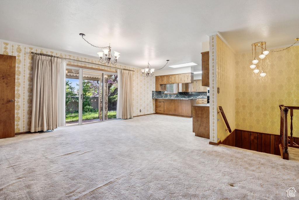 Unfurnished living room featuring wallpapered walls, a chandelier, and light colored carpet