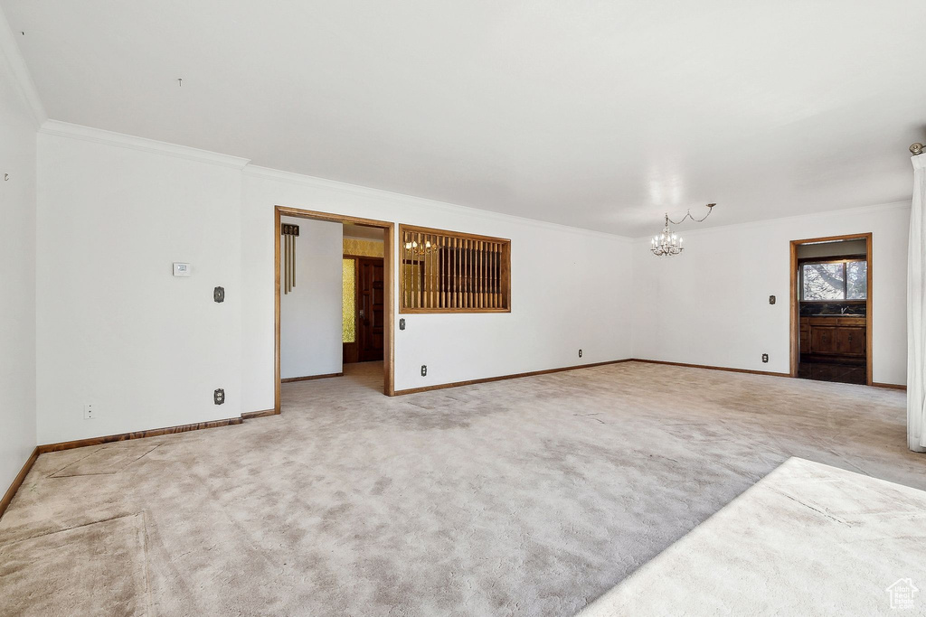 Carpeted spare room with a chandelier, baseboards, and crown molding