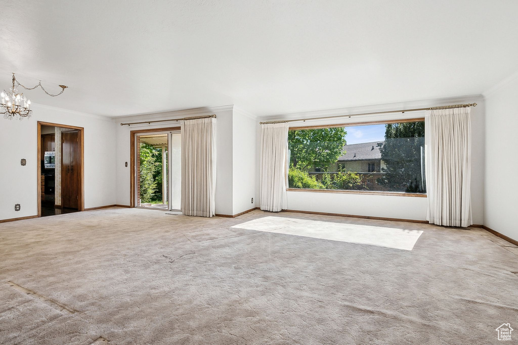 Carpeted empty room with a chandelier, baseboards, and ornamental molding
