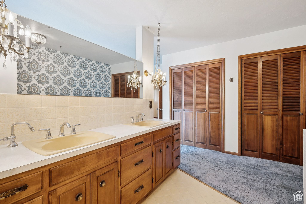 Full bath with a chandelier, double vanity, decorative backsplash, and a closet