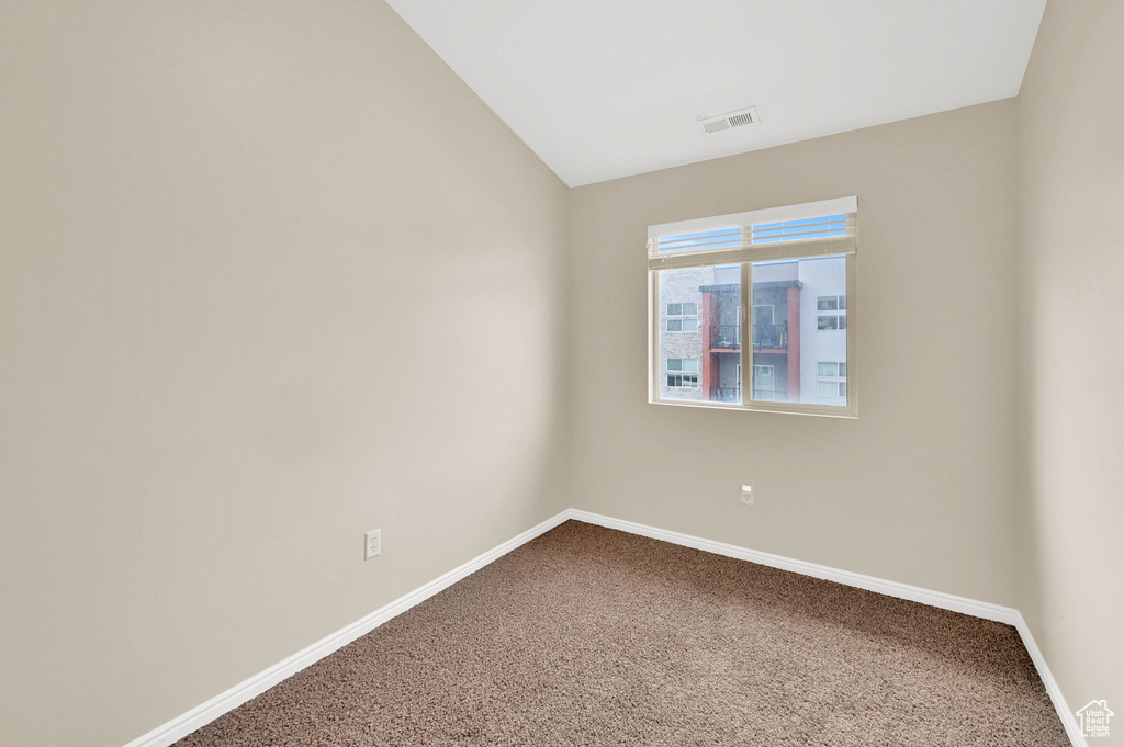 Empty room with dark colored carpet, baseboards, and vaulted ceiling