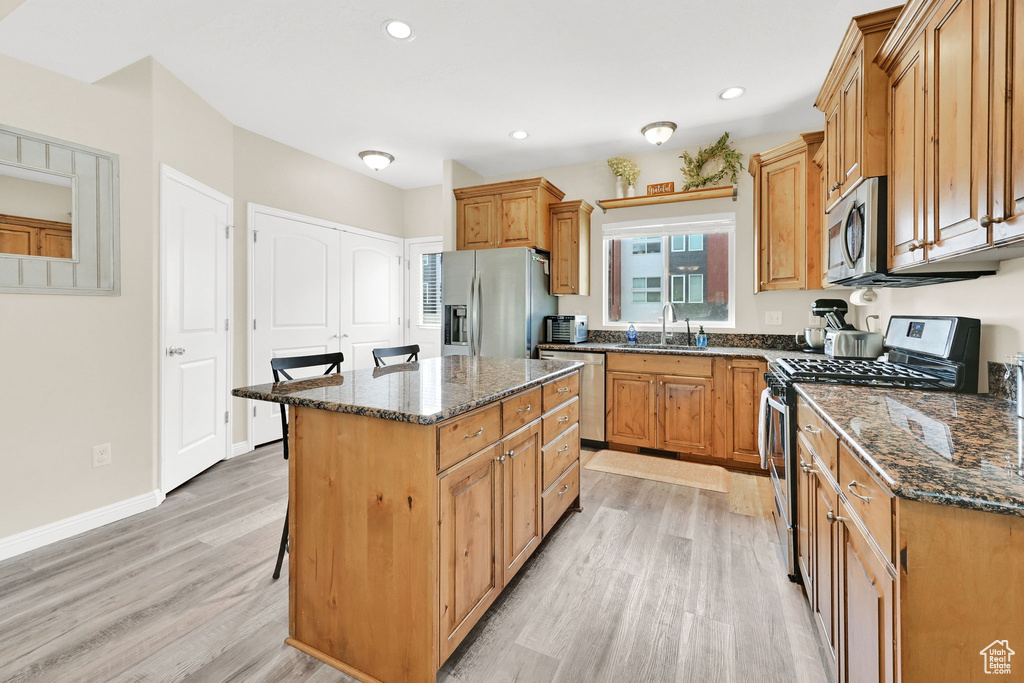 Kitchen featuring appliances with stainless steel finishes, a sink, light wood-style floors, a kitchen bar, and dark stone countertops