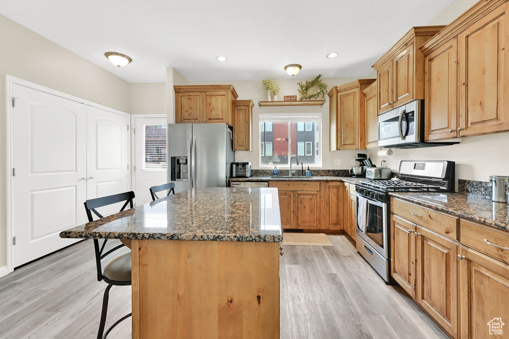 Kitchen featuring appliances with stainless steel finishes, a kitchen bar, a sink, light wood-style floors, and recessed lighting