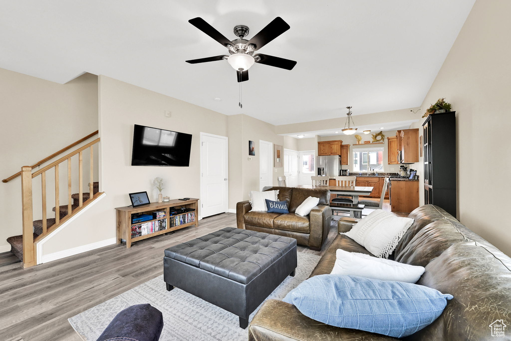 Living room with light wood finished floors, stairs, a ceiling fan, and baseboards