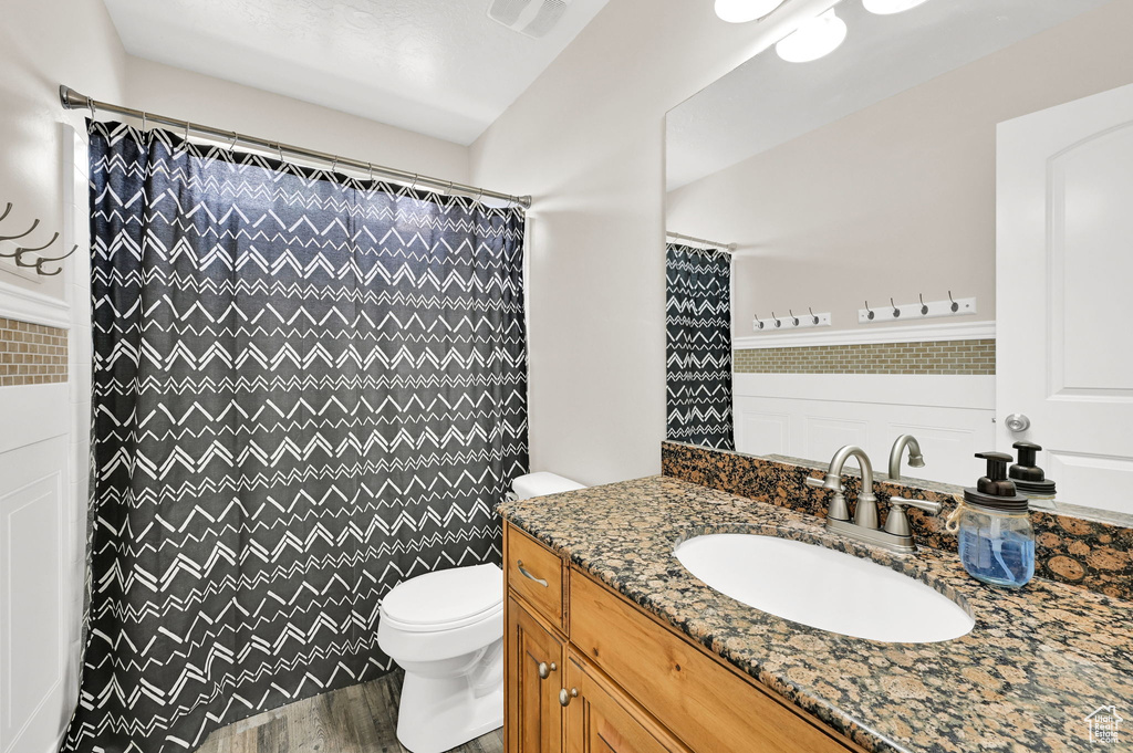 Full bathroom featuring toilet, wood finished floors, vanity, and curtained shower