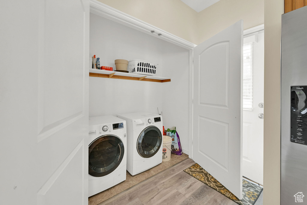 Clothes washing area with washing machine and clothes dryer and light wood-style floors