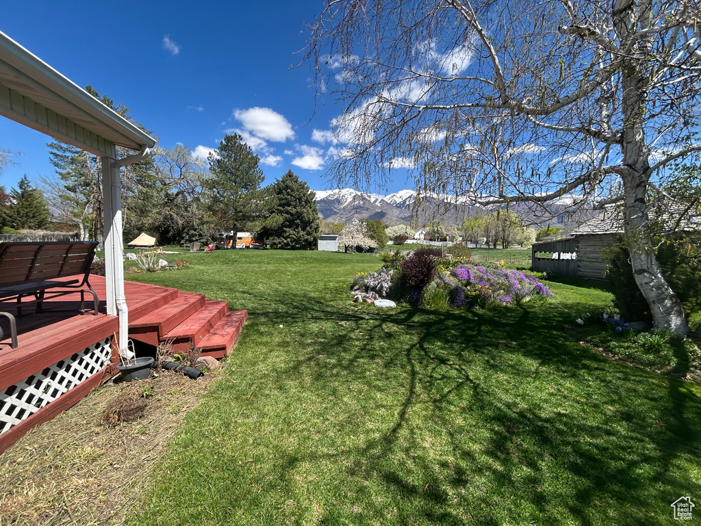 View of grassy yard with a deck with mountain view