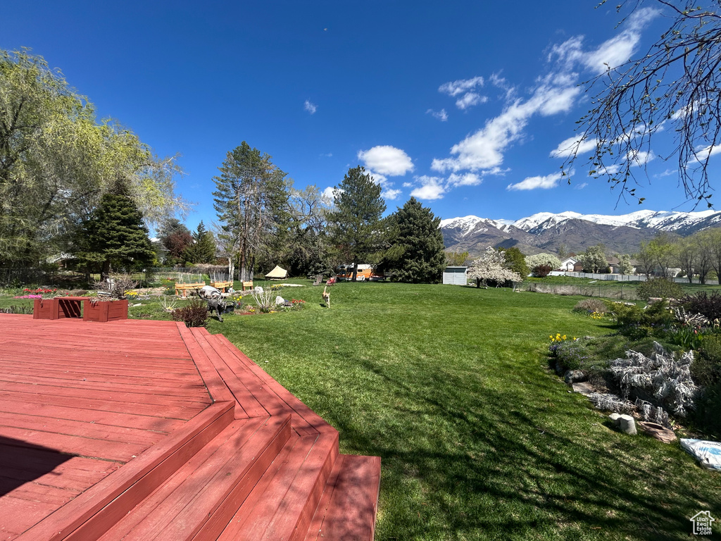 View of grassy yard with a deck with mountain view