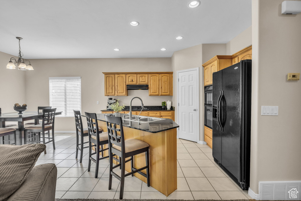 Kitchen with black fridge, under cabinet range hood, a breakfast bar, light tile patterned floors, and a sink