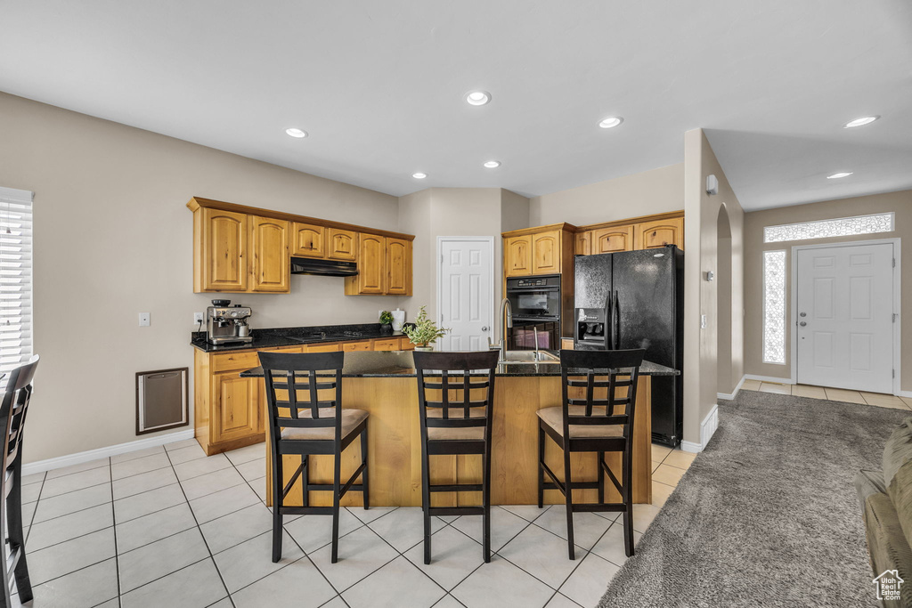Kitchen with under cabinet range hood, black appliances, light tile patterned floors, a breakfast bar area, and recessed lighting