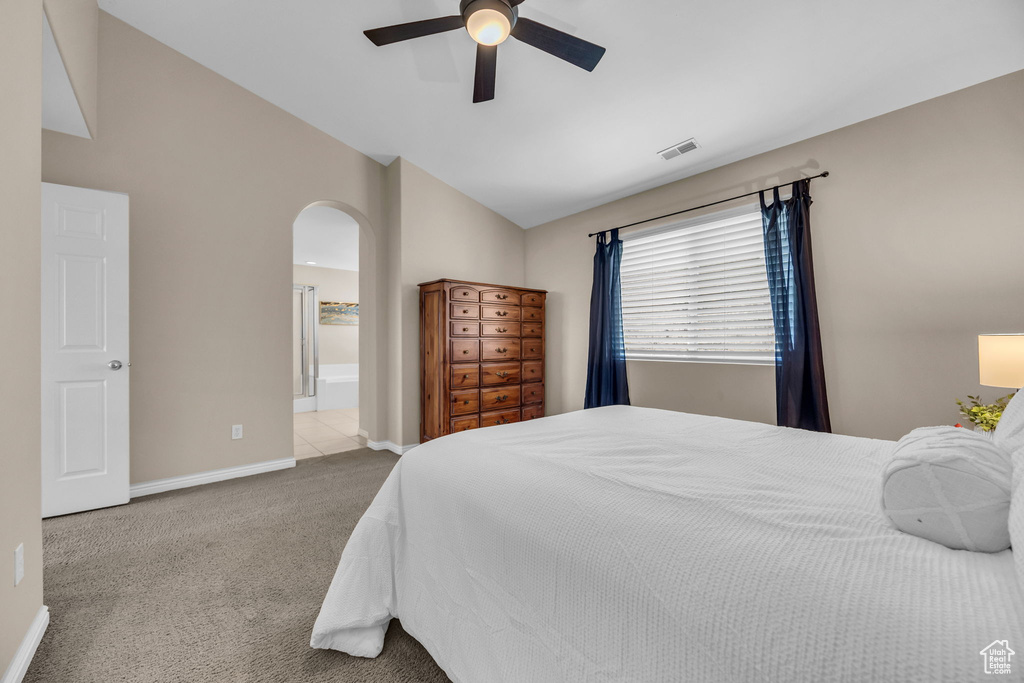 Carpeted bedroom featuring lofted ceiling, arched walkways, baseboards, ceiling fan, and ensuite bath
