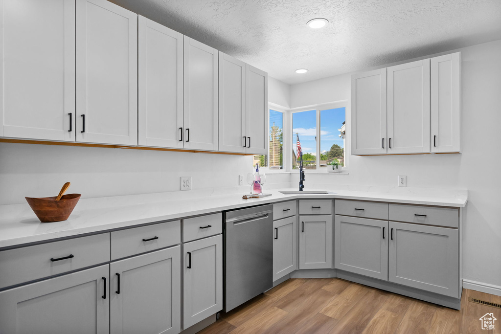 Kitchen with stainless steel dishwasher, a sink, a textured ceiling, light wood-style flooring, and gray cabinets