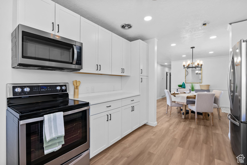 Kitchen with stainless steel appliances, white cabinets, a chandelier, light wood finished floors, and light countertops