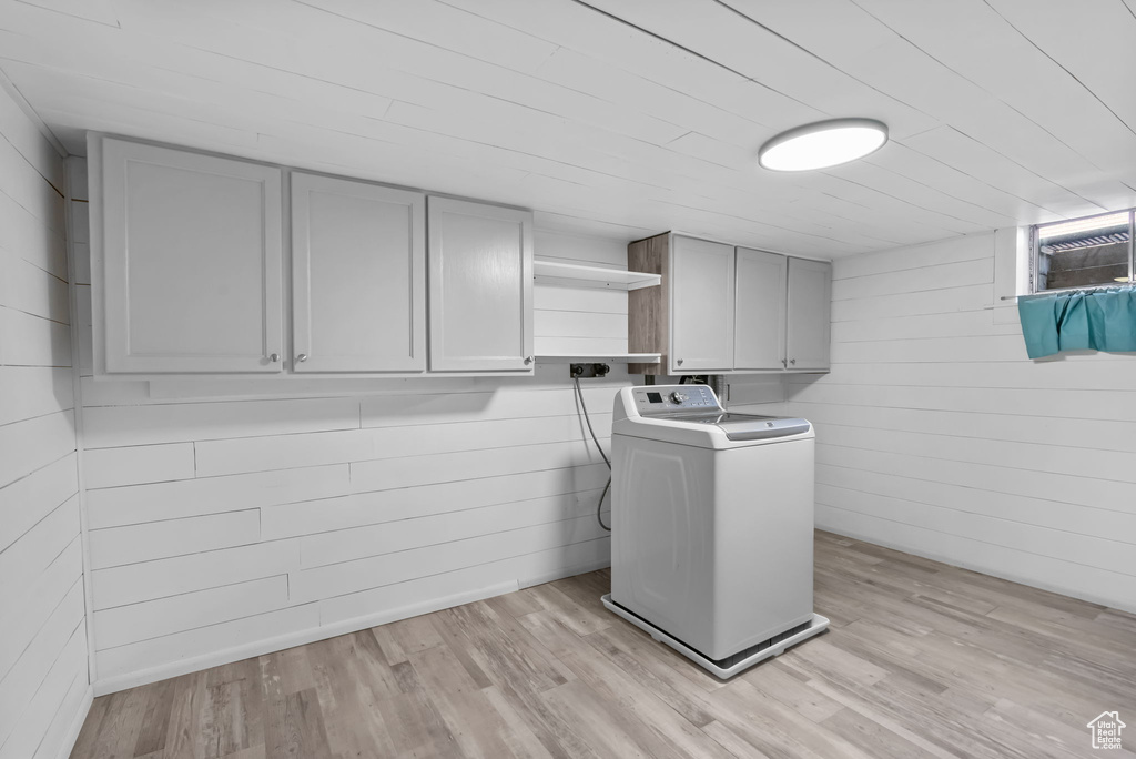 Laundry room featuring washer / dryer, cabinet space, light wood-style flooring, and wooden walls