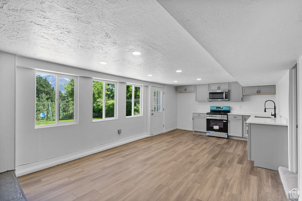 Kitchen with stainless steel appliances, gray cabinets, a sink, light countertops, and healthy amount of natural light