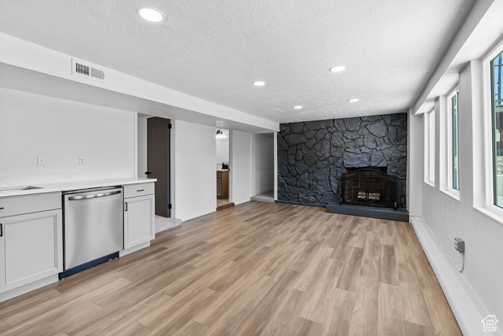 Unfurnished living room with a textured ceiling, light wood finished floors, a stone fireplace, recessed lighting, and baseboards