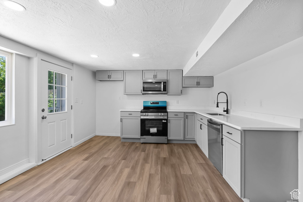 Kitchen with gray cabinetry, stainless steel appliances, a sink, a textured ceiling, and light wood finished floors