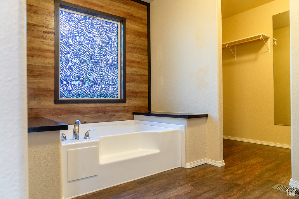 Bathroom with wooden walls, wood finished floors, a garden tub, a spacious closet, and baseboards