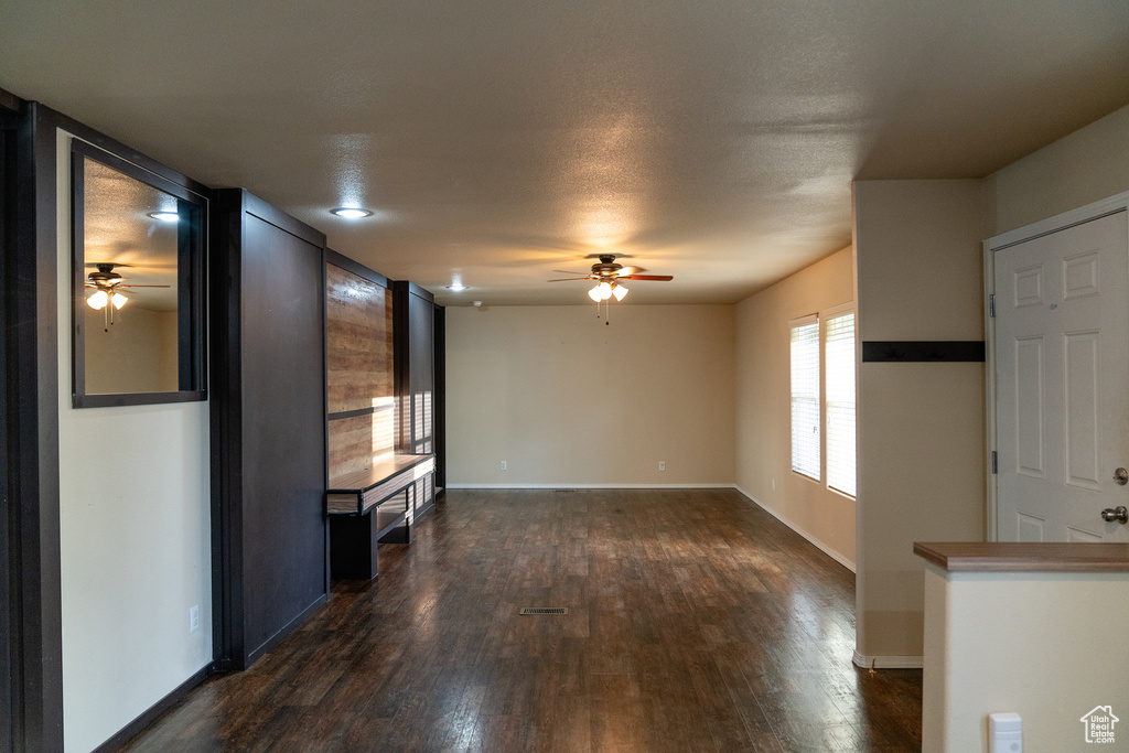Unfurnished living room with a ceiling fan, dark wood-style floors, and baseboards