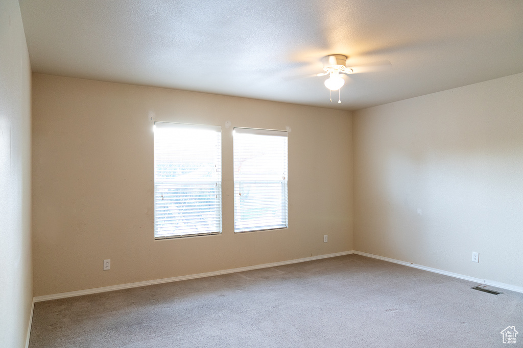 Carpeted spare room featuring ceiling fan and baseboards