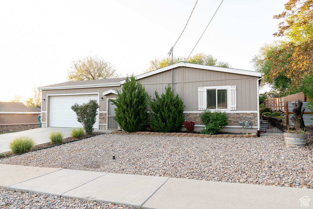 View of front facade featuring stone siding, concrete driveway, a garage, and fence