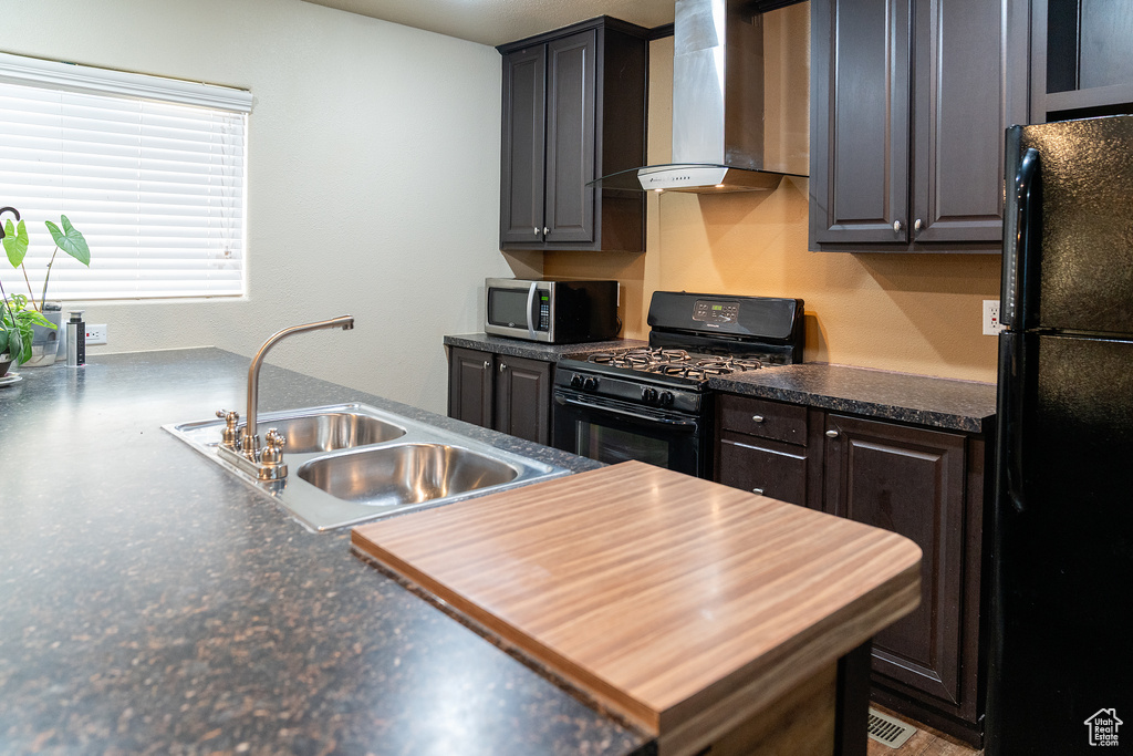 Kitchen with black appliances, wall chimney exhaust hood, a sink, and dark countertops