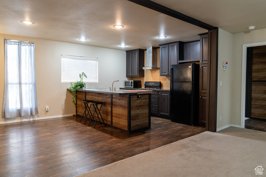Kitchen with freestanding refrigerator, wall chimney range hood, a peninsula, a breakfast bar, and recessed lighting