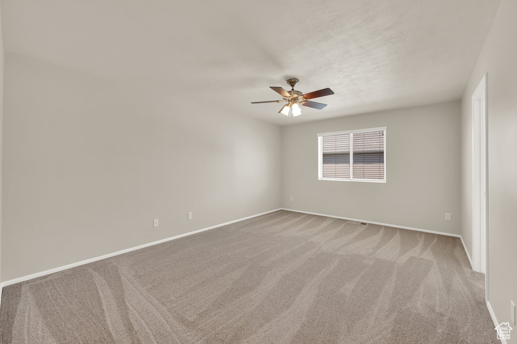 Spare room featuring ceiling fan, light carpet, and baseboards