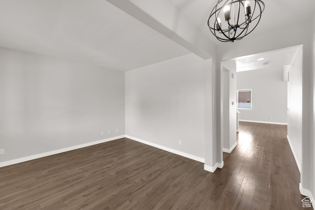 Unfurnished dining area featuring a chandelier, dark wood-type flooring, and baseboards