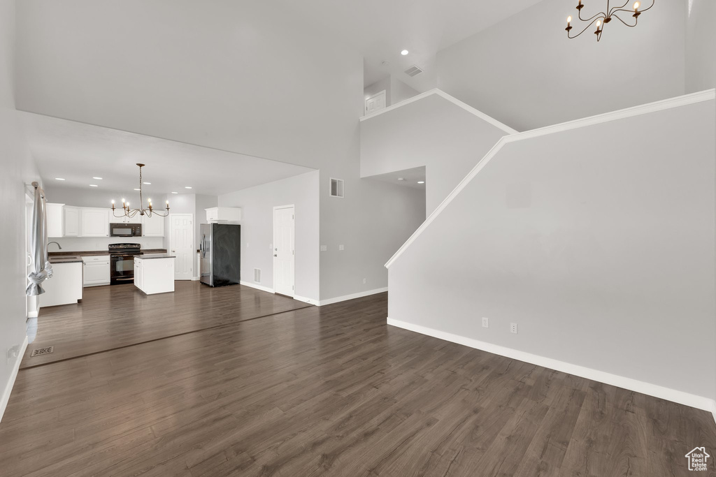 Unfurnished living room featuring a chandelier, baseboards, recessed lighting, dark wood-type flooring, and a high ceiling