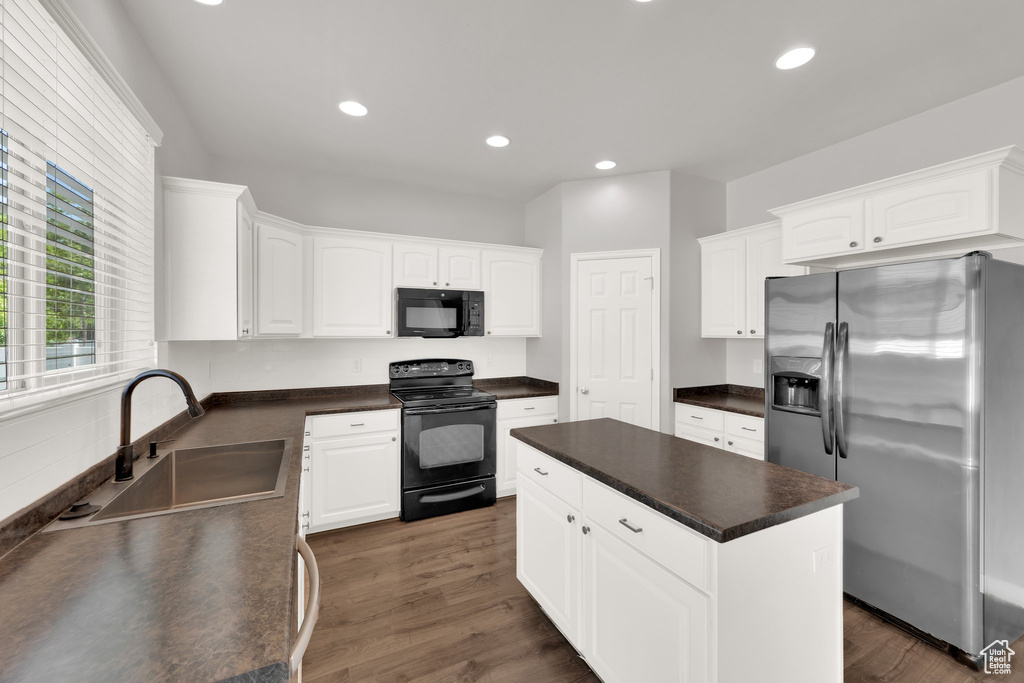 Kitchen with black appliances, a sink, dark countertops, a kitchen island, and white cabinets