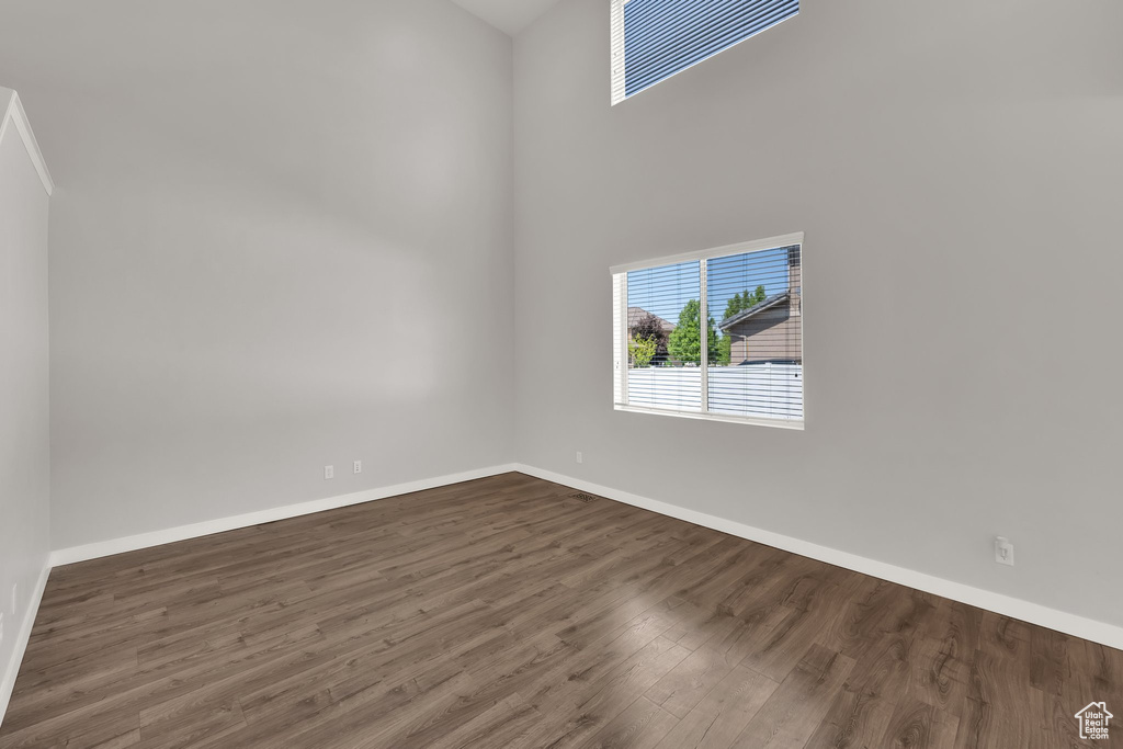 Unfurnished room with dark wood finished floors, baseboards, and a towering ceiling