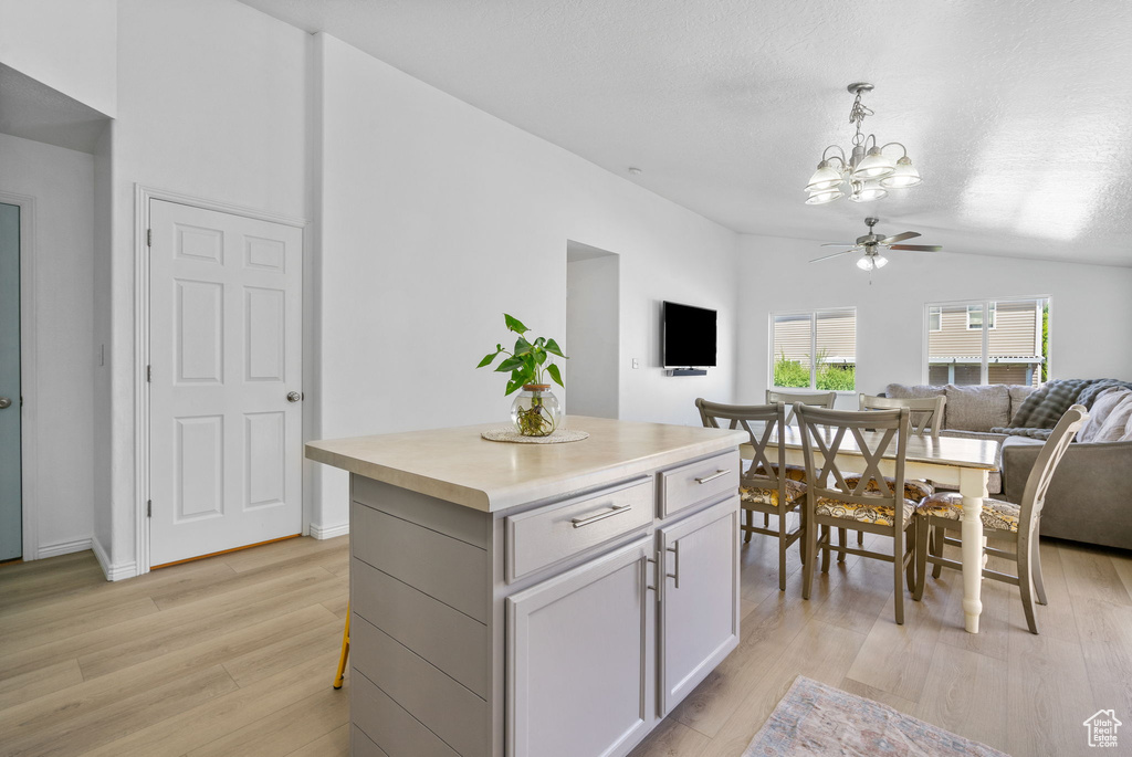Kitchen with open floor plan, lofted ceiling, light wood finished floors, a chandelier, and pendant lighting