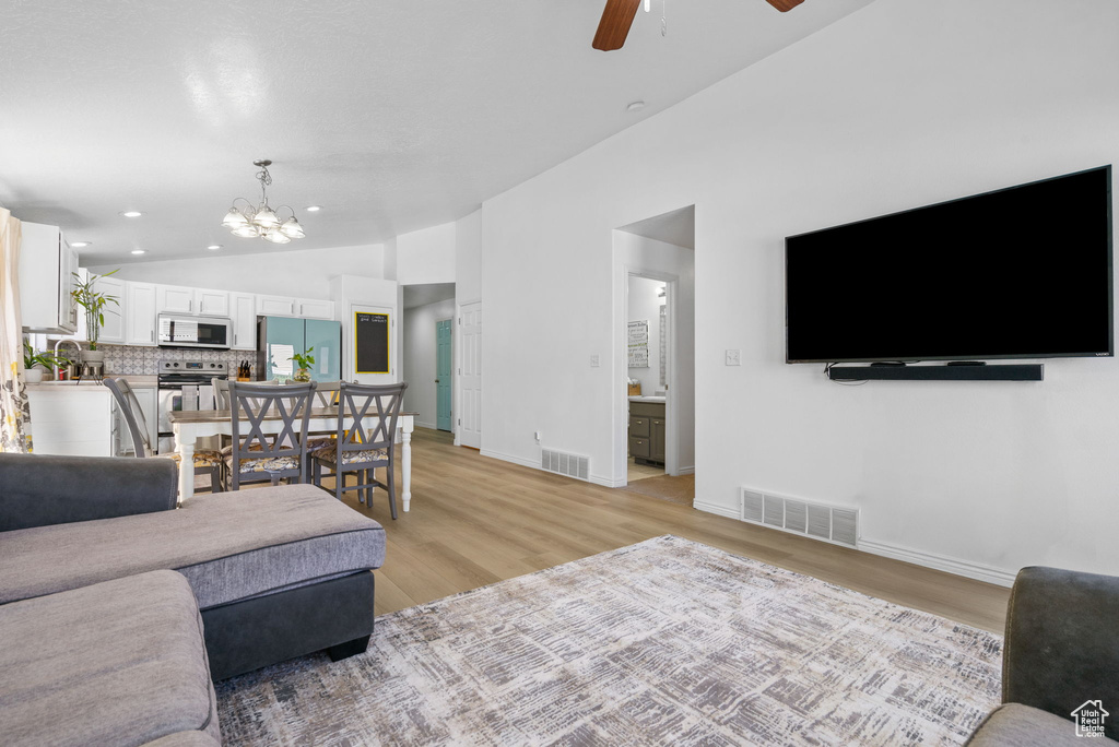 Living area with vaulted ceiling, ceiling fan, light wood-type flooring, a chandelier, and baseboards