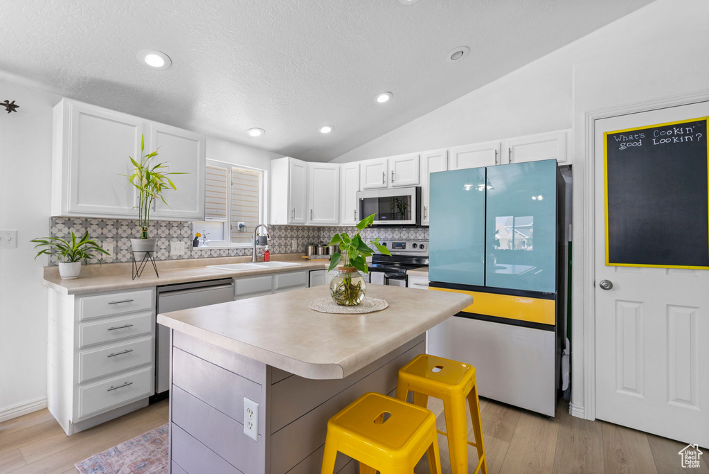 Kitchen featuring appliances with stainless steel finishes, a sink, white cabinets, tasteful backsplash, and light wood finished floors