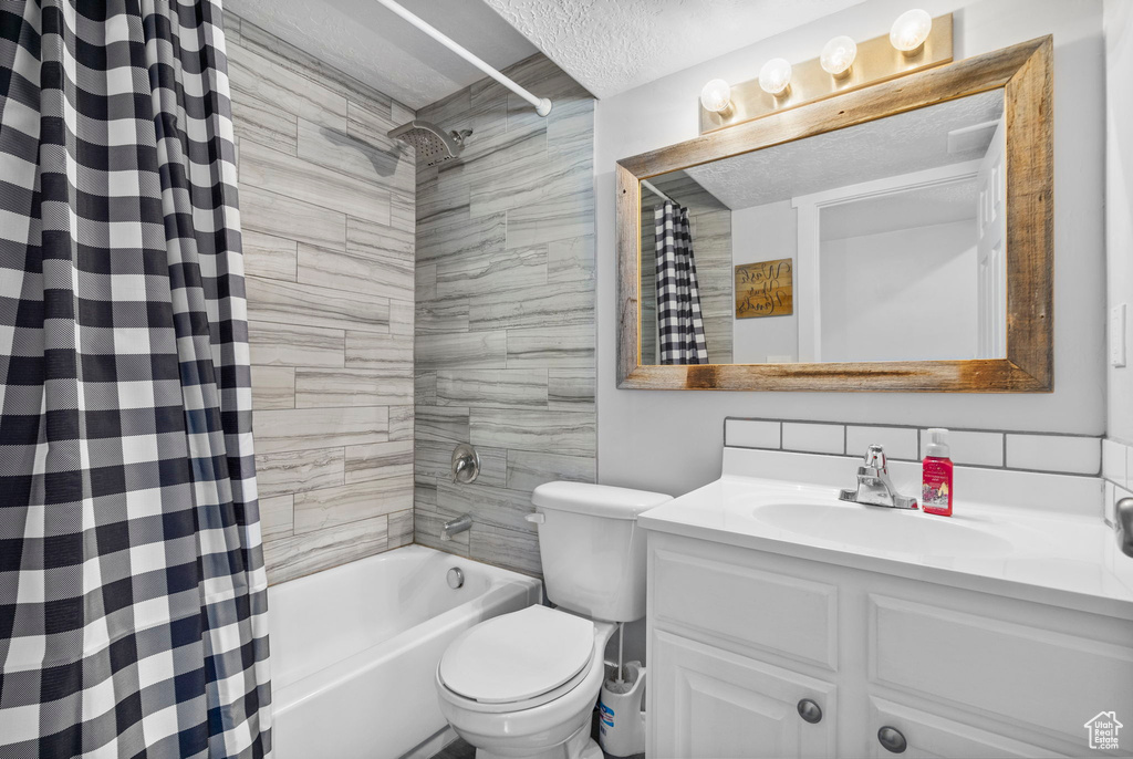 Bathroom featuring toilet, vanity, shower / bath combo with shower curtain, and a textured ceiling