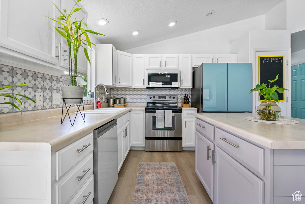 Kitchen with appliances with stainless steel finishes, a sink, white cabinetry, light countertops, and decorative backsplash