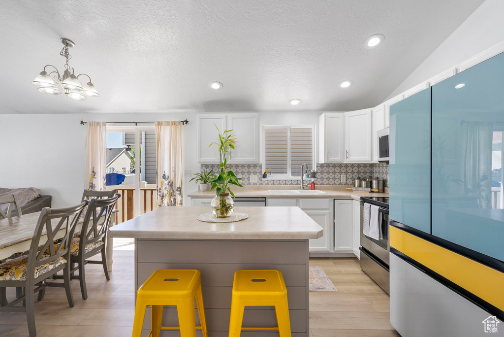Kitchen with stainless steel range with electric stovetop, a sink, backsplash, white cabinets, and white microwave