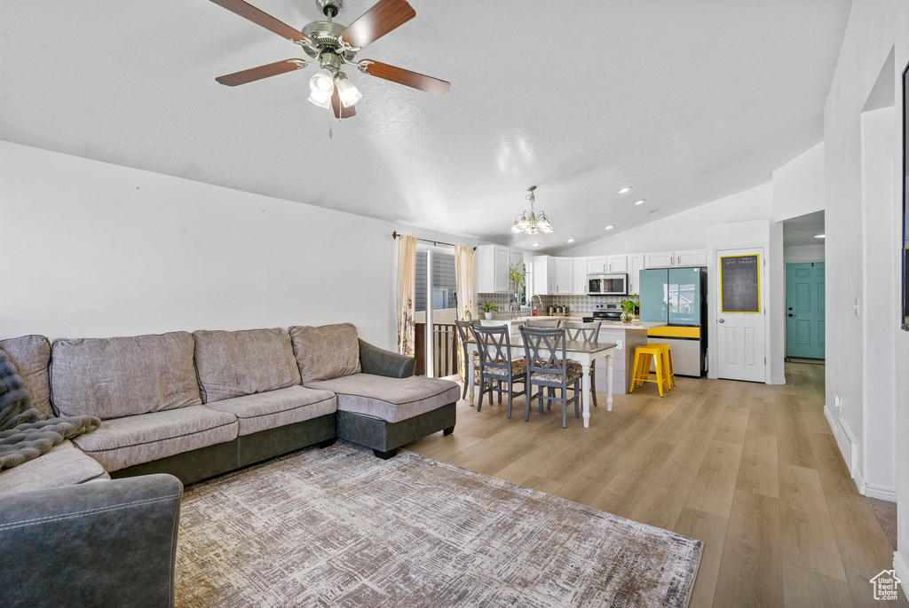 Living area with vaulted ceiling, a chandelier, light wood-style flooring, ceiling fan, and recessed lighting