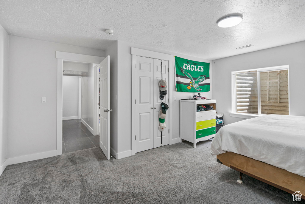 Bedroom with a textured ceiling, carpet flooring, baseboards, and a closet