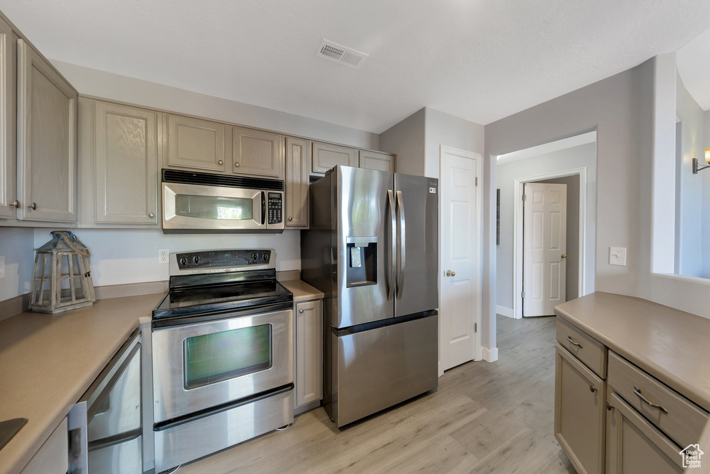 Kitchen featuring stainless steel appliances, light countertops, light wood-style flooring, and cream cabinetry