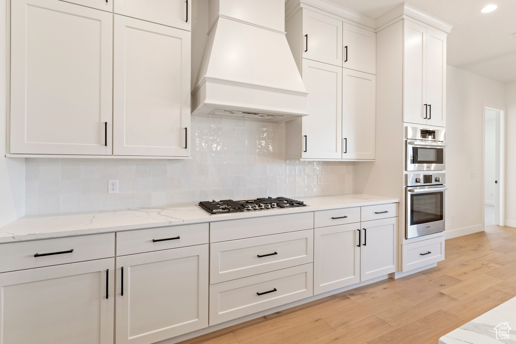 Kitchen featuring custom exhaust hood, stainless steel appliances, light wood-style floors, backsplash, and recessed lighting