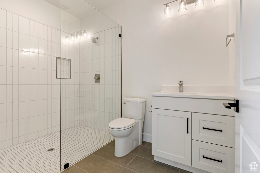 Bathroom with a walk in shower, vanity, tile patterned flooring, and toilet