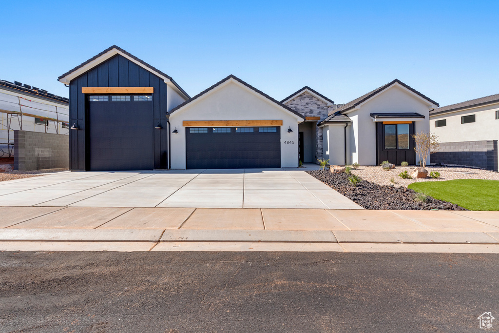 View of front of home with an attached garage, concrete driveway, board and batten siding, and stucco siding