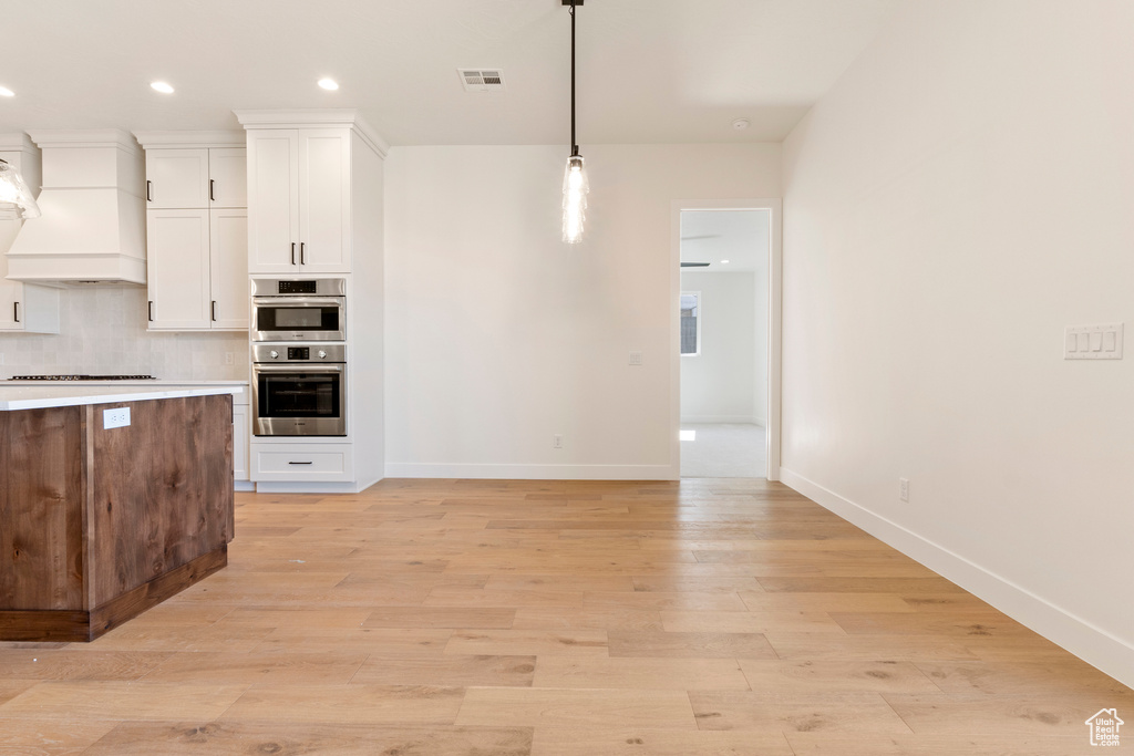 Kitchen with custom exhaust hood, white cabinetry, baseboards, pendant lighting, and recessed lighting