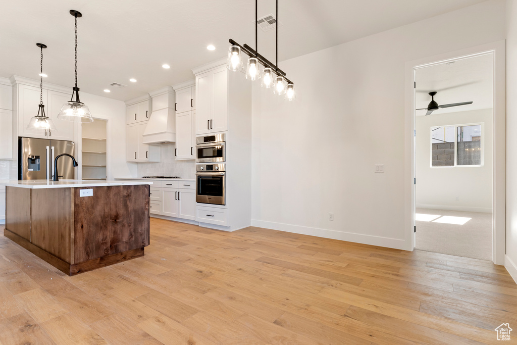 Kitchen with stainless steel appliances, custom range hood, light countertops, light wood-type flooring, and recessed lighting