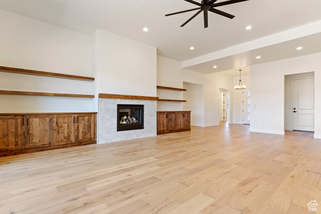 Unfurnished living room featuring a chandelier, a ceiling fan, light wood-type flooring, a tiled fireplace, and recessed lighting