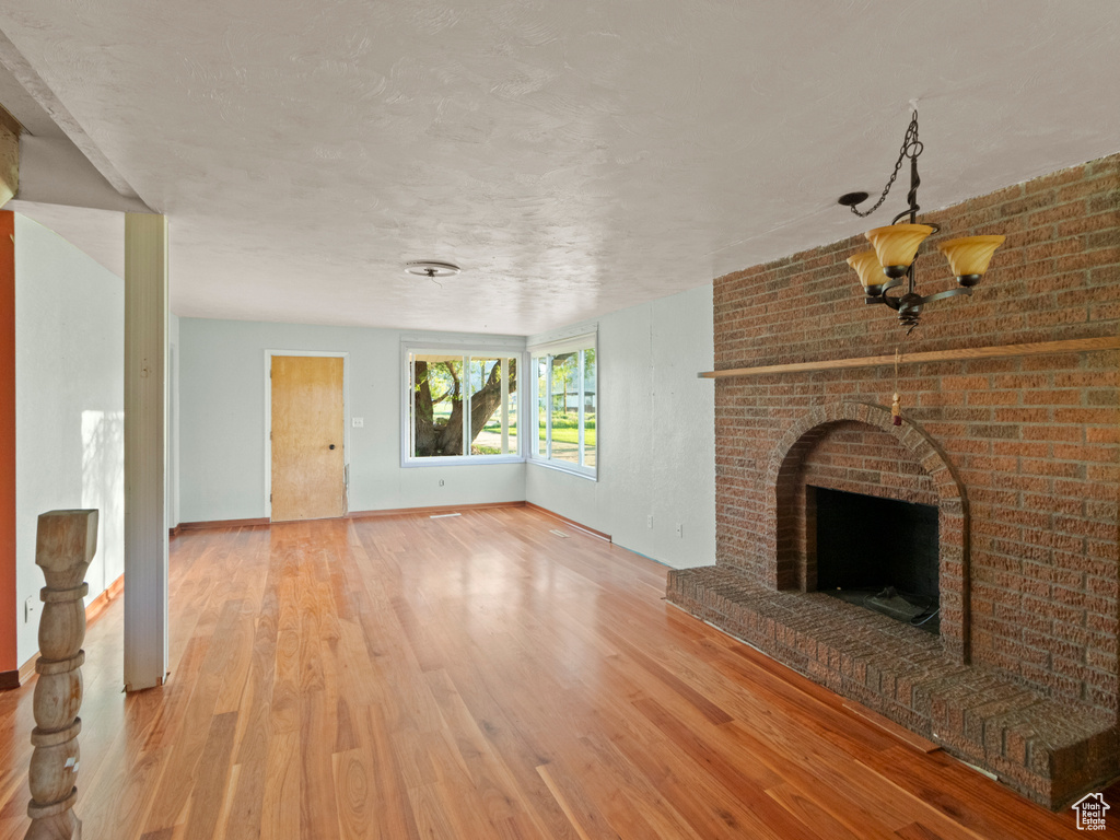 Unfurnished living room featuring wood finished floors, a fireplace, baseboards, and a textured ceiling