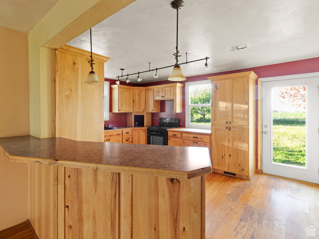 Kitchen with black gas stove, a peninsula, light wood-type flooring, and light brown cabinetry