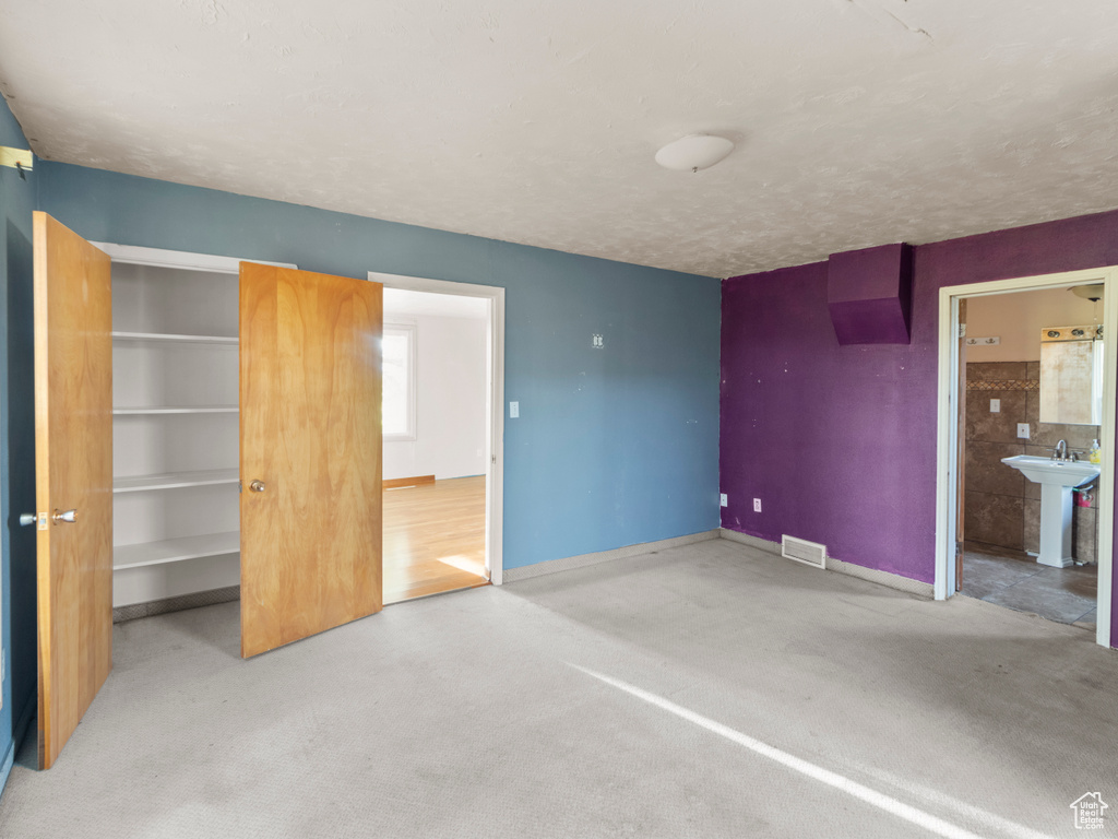 Unfurnished bedroom featuring a sink, baseboards, connected bathroom, a walk in closet, and a closet